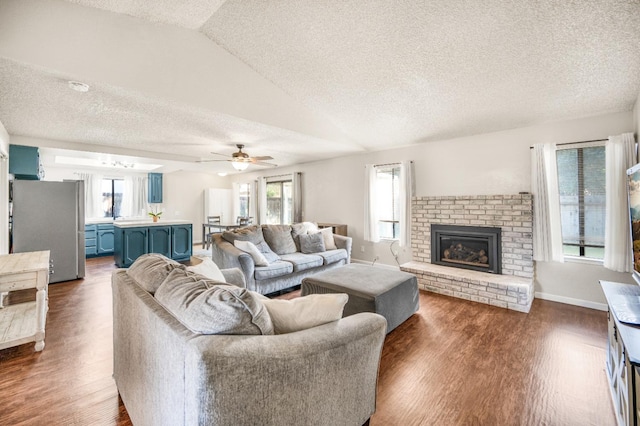 living room featuring a textured ceiling, ceiling fan, a fireplace, plenty of natural light, and lofted ceiling