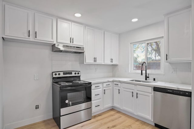 kitchen featuring appliances with stainless steel finishes, white cabinets, a sink, light stone countertops, and under cabinet range hood