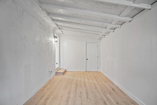 unfurnished room featuring beam ceiling, baseboards, and wood finished floors