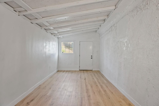 spare room featuring baseboards, vaulted ceiling with beams, and light wood finished floors