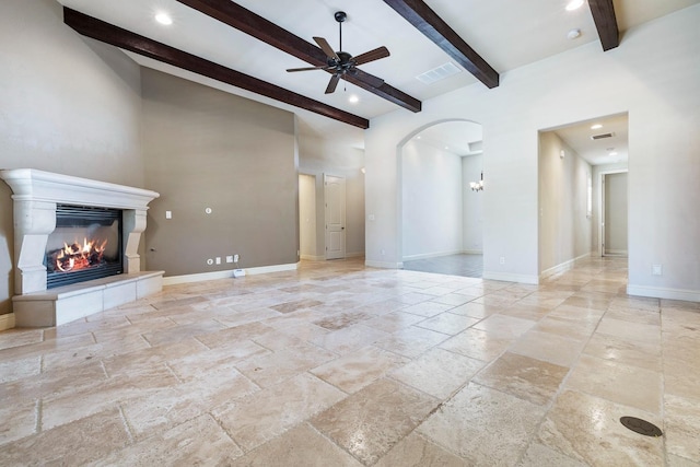 10810 N Matus Ave, Fresno, CA 93730 - unfurnished living room with beam ceiling, arched walkways, a glass covered fireplace, a ceiling fan, and stone tile flooring