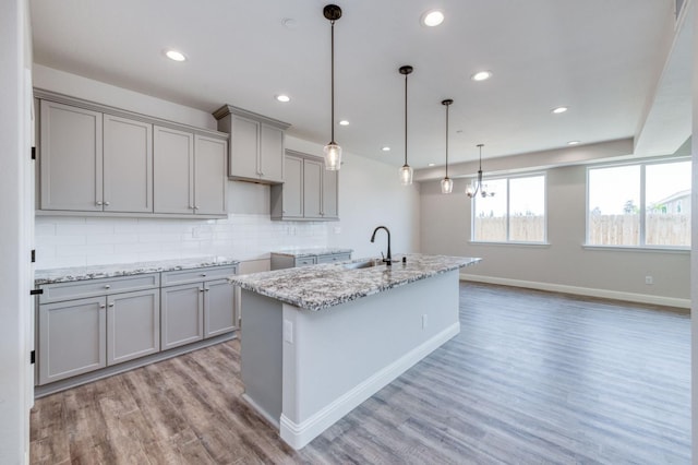 kitchen featuring pendant lighting, gray cabinets, light stone counters, and an island with sink