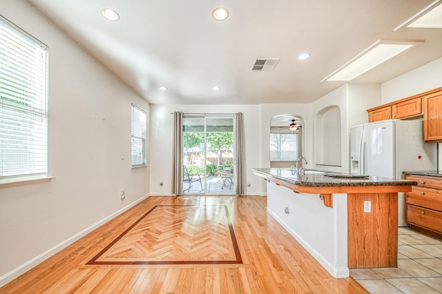 kitchen featuring a kitchen island with sink, white fridge with ice dispenser, a breakfast bar area, ceiling fan, and sink