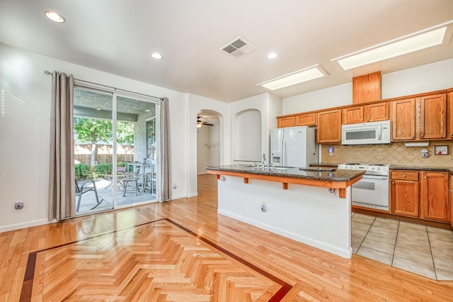 kitchen featuring white appliances, a kitchen island with sink, a breakfast bar area, ceiling fan, and sink