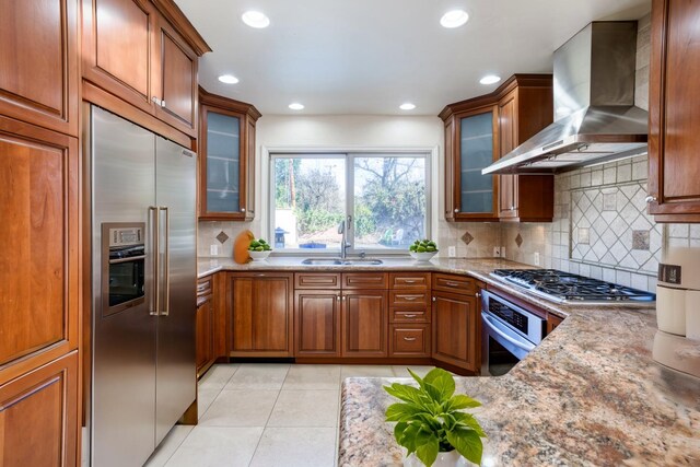 3628 N Van Ness, Fresno, CA 93704 - kitchen with appliances with stainless steel finishes, wall chimney exhaust hood, brown cabinets, light stone countertops, and light tile patterned floors