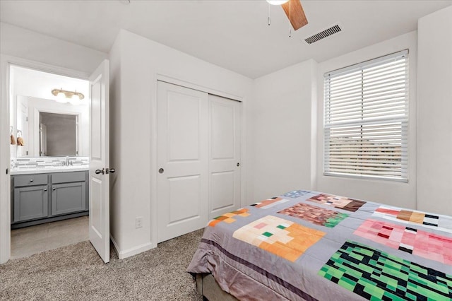 carpeted bedroom with ceiling fan, a closet, ensuite bathroom, and sink