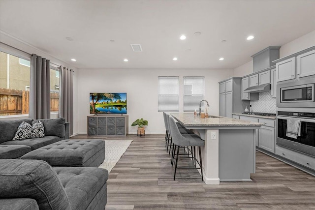 kitchen featuring gray cabinetry, stainless steel appliances, tasteful backsplash, an island with sink, and hardwood / wood-style flooring