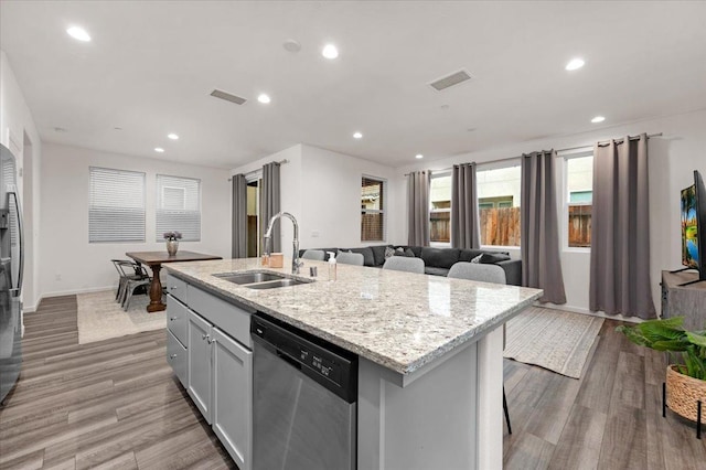 kitchen featuring sink, light stone counters, light hardwood / wood-style flooring, stainless steel dishwasher, and a center island with sink