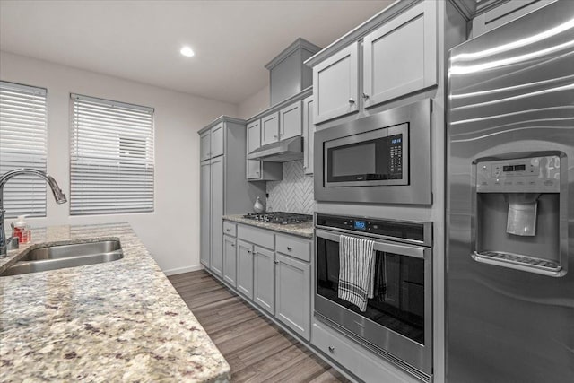 kitchen with sink, gray cabinets, appliances with stainless steel finishes, tasteful backsplash, and light stone counters