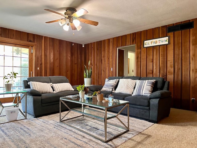 living room featuring carpet flooring, a textured ceiling, ceiling fan, and wood walls