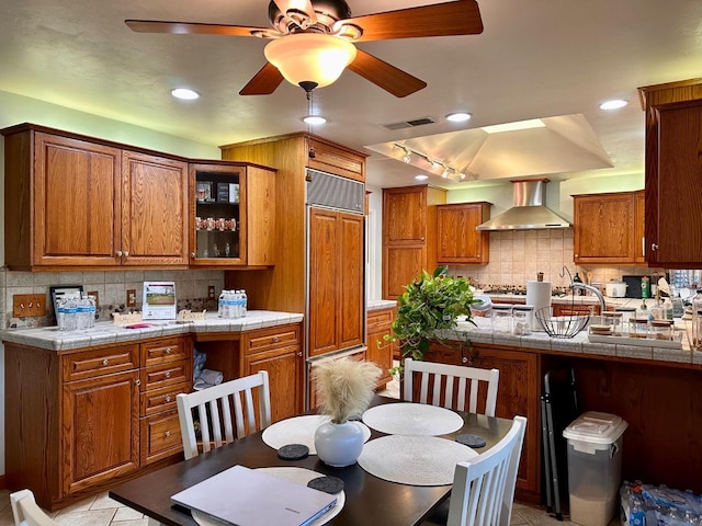 kitchen with tasteful backsplash, tile countertops, paneled fridge, and wall chimney range hood