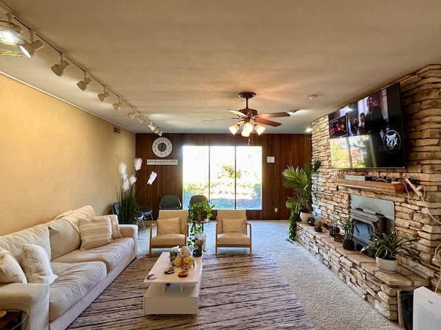 carpeted living room with ceiling fan, wooden walls, and a wood stove