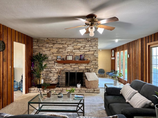 carpeted living room featuring ceiling fan, a stone fireplace, a textured ceiling, and wood walls