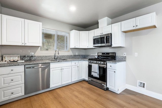 kitchen featuring sink, light hardwood / wood-style flooring, dark stone countertops, appliances with stainless steel finishes, and white cabinetry