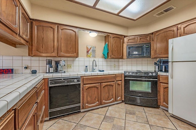 kitchen with sink, tasteful backsplash, tile countertops, light tile patterned floors, and black appliances