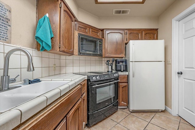 kitchen with black appliances, sink, tasteful backsplash, tile counters, and light tile patterned flooring