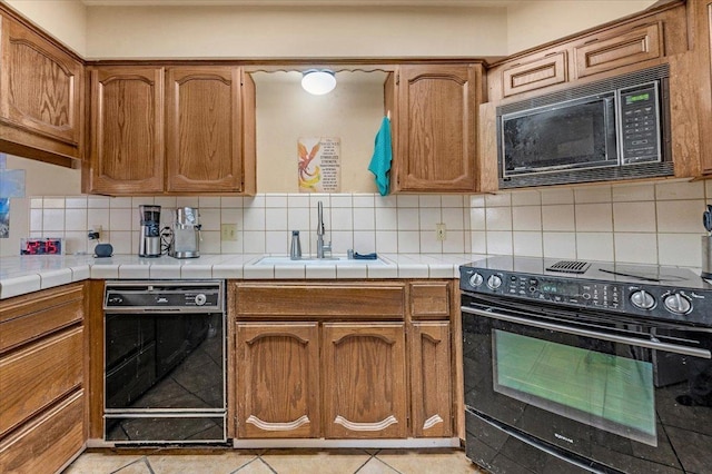 kitchen with black appliances, tasteful backsplash, sink, and tile countertops