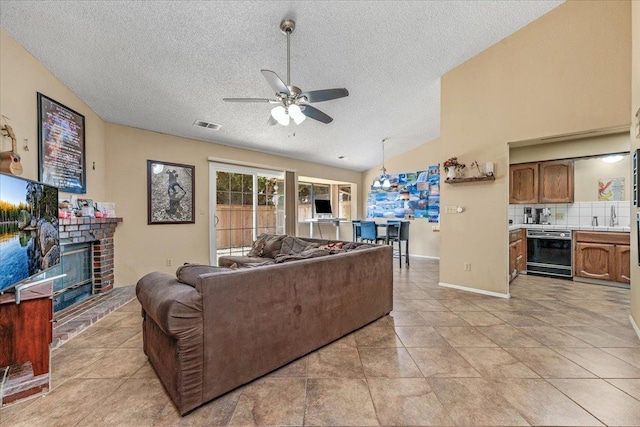 living room with ceiling fan, a textured ceiling, lofted ceiling, a fireplace, and light tile patterned flooring