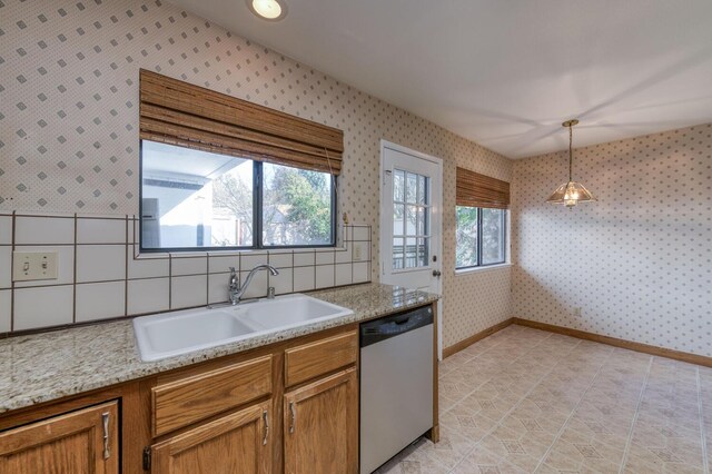 kitchen featuring light stone counters, sink, hanging light fixtures, and dishwasher