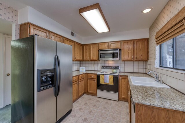 kitchen with tasteful backsplash, appliances with stainless steel finishes, sink, and light stone counters