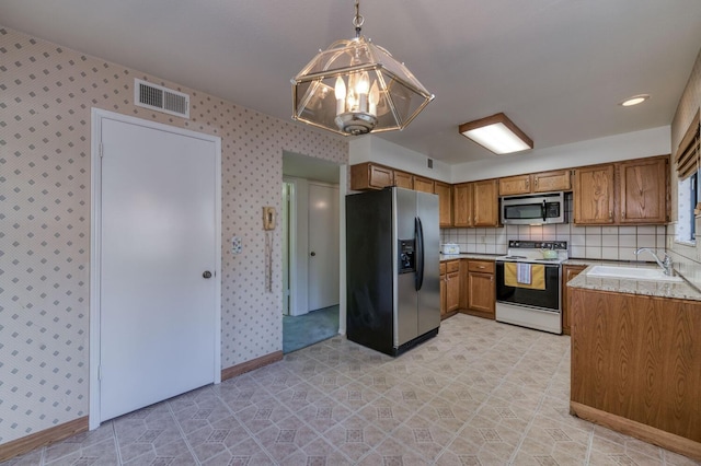 kitchen with appliances with stainless steel finishes, sink, hanging light fixtures, and backsplash