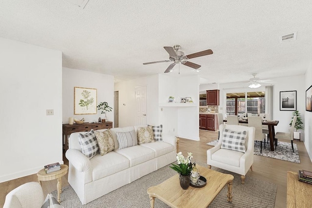 living room with a textured ceiling, light hardwood / wood-style flooring, and ceiling fan