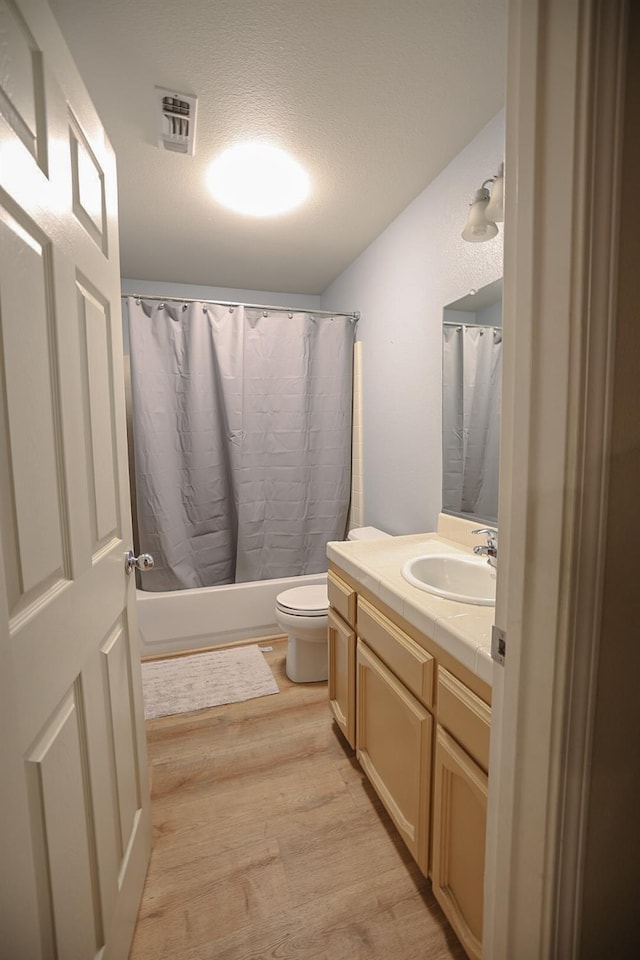 full bathroom with shower / bathtub combination with curtain, a textured ceiling, toilet, vanity, and hardwood / wood-style flooring