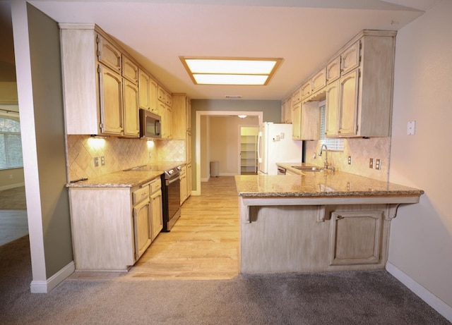 kitchen with kitchen peninsula, light stone counters, stainless steel appliances, sink, and light brown cabinets