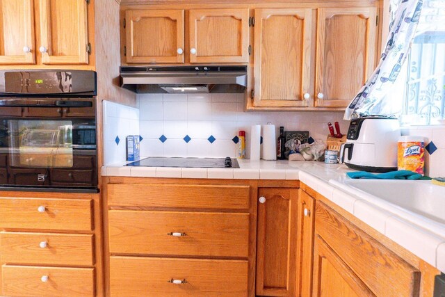 kitchen with sink, tile counters, black appliances, and tasteful backsplash