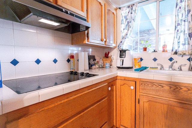 kitchen featuring tile countertops, range hood, sink, tasteful backsplash, and black electric stovetop