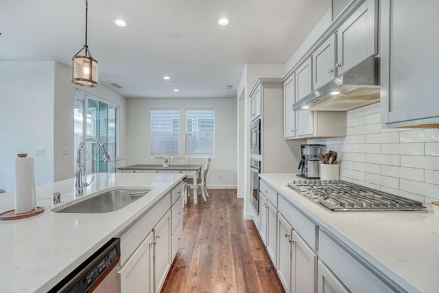 kitchen with sink, stainless steel appliances, dark wood-type flooring, light stone counters, and pendant lighting