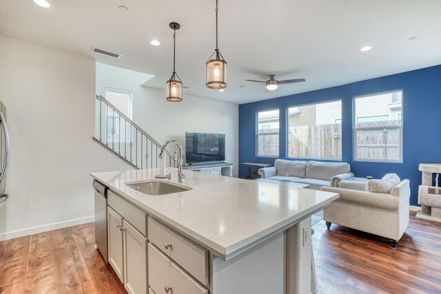 kitchen with light stone counters, sink, dishwasher, hanging light fixtures, and an island with sink