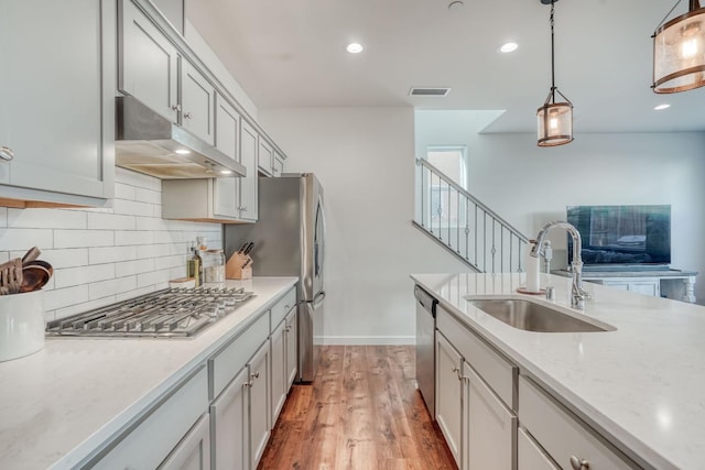 kitchen with appliances with stainless steel finishes, tasteful backsplash, sink, hardwood / wood-style floors, and hanging light fixtures