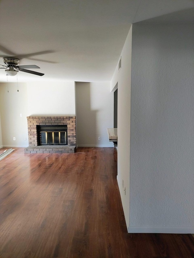 unfurnished living room featuring ceiling fan, a fireplace, and dark wood-type flooring