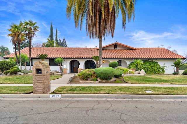 mediterranean / spanish-style home featuring concrete driveway, a tile roof, a front lawn, and stucco siding