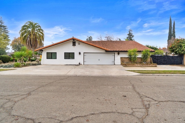 mediterranean / spanish home featuring a tile roof, stucco siding, fence, a garage, and driveway