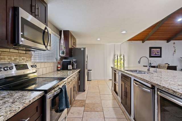 kitchen with light stone counters, tasteful backsplash, appliances with stainless steel finishes, a sink, and beverage cooler