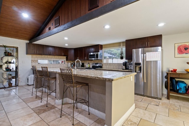 kitchen with a center island, sink, appliances with stainless steel finishes, light stone counters, and a breakfast bar area