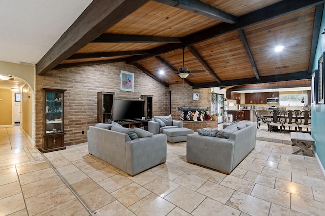 living area featuring arched walkways, ceiling fan, lofted ceiling with beams, wooden ceiling, and brick wall