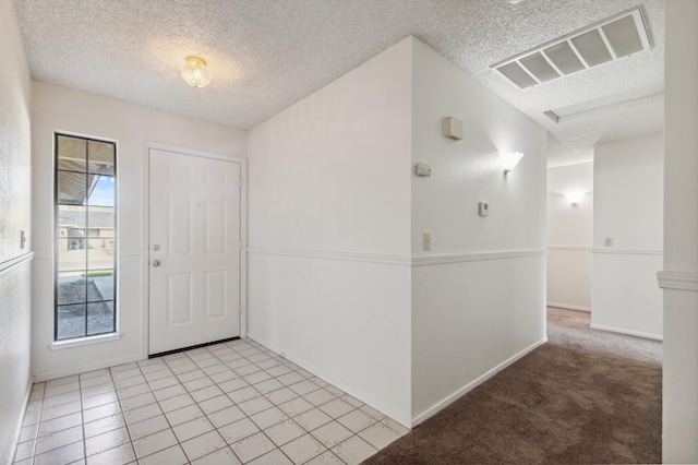 foyer entrance with light tile patterned floors, light colored carpet, visible vents, a textured ceiling, and baseboards