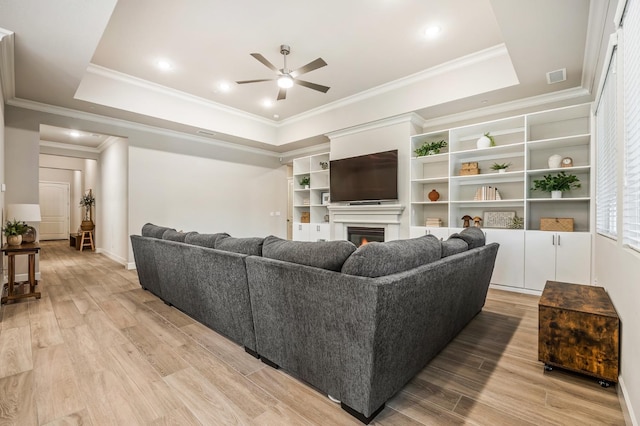 living room featuring a raised ceiling, ceiling fan, light hardwood / wood-style flooring, and ornamental molding