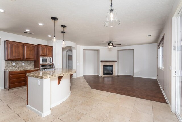 kitchen featuring sink, a tile fireplace, pendant lighting, a center island with sink, and stainless steel microwave