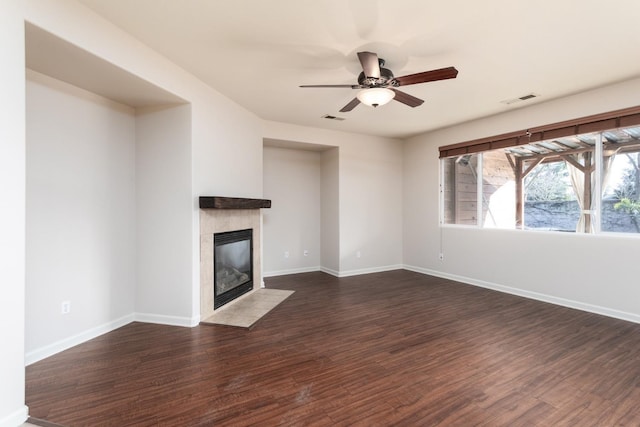 unfurnished living room with ceiling fan, dark wood-type flooring, and a tile fireplace