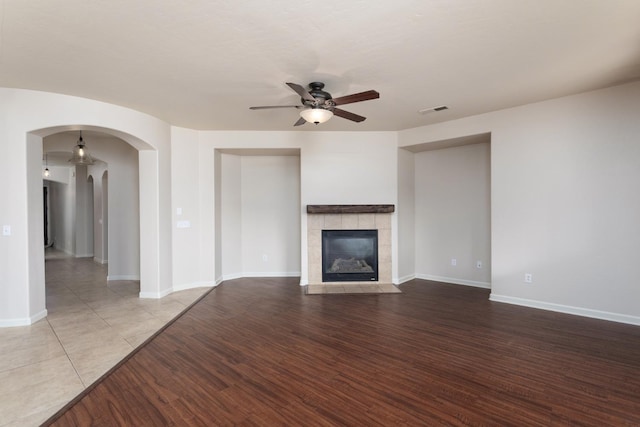 unfurnished living room with ceiling fan, wood-type flooring, and a tile fireplace