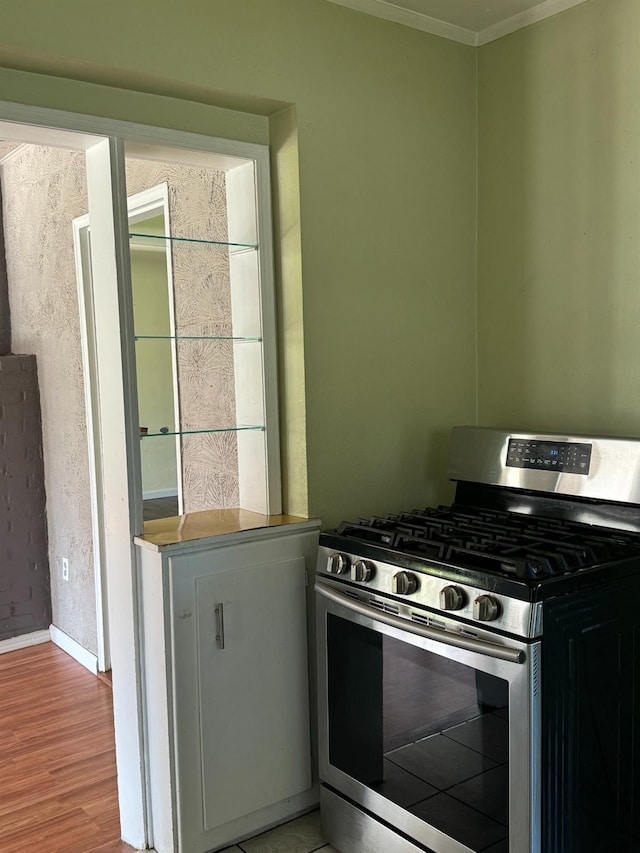 kitchen with light wood-type flooring, ornamental molding, and gas range