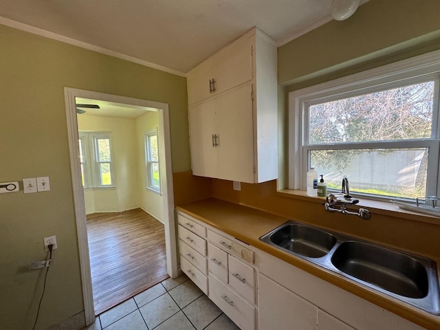 kitchen featuring light tile patterned floors, white cabinetry, crown molding, and sink