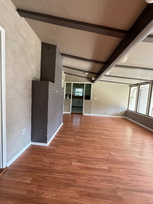 unfurnished living room featuring hardwood / wood-style floors, lofted ceiling with beams, and a textured ceiling