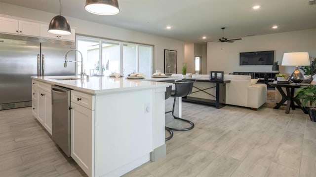 kitchen with a center island with sink, decorative light fixtures, white cabinetry, and appliances with stainless steel finishes