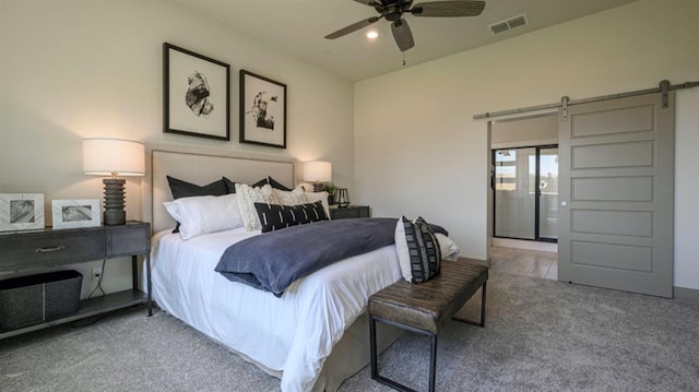 bedroom with ceiling fan, a barn door, and light carpet