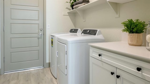 clothes washing area with cabinets, light wood-type flooring, and separate washer and dryer